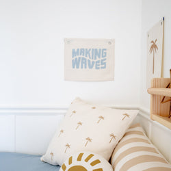 Cozy nautical-themed bedroom decor with "Making Waves" wall art and palm tree patterned cushions.