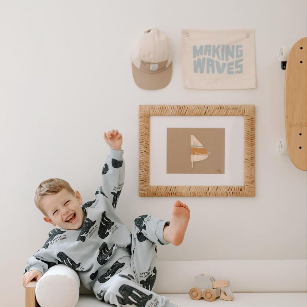 Young child in playful pajamas laughing in a stylish kids' room with wall decor and skateboard.