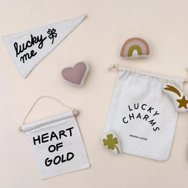 Lucky charms and accessories including a pouch, heart shape, rainbow, and banners with positive messages on a beige background.