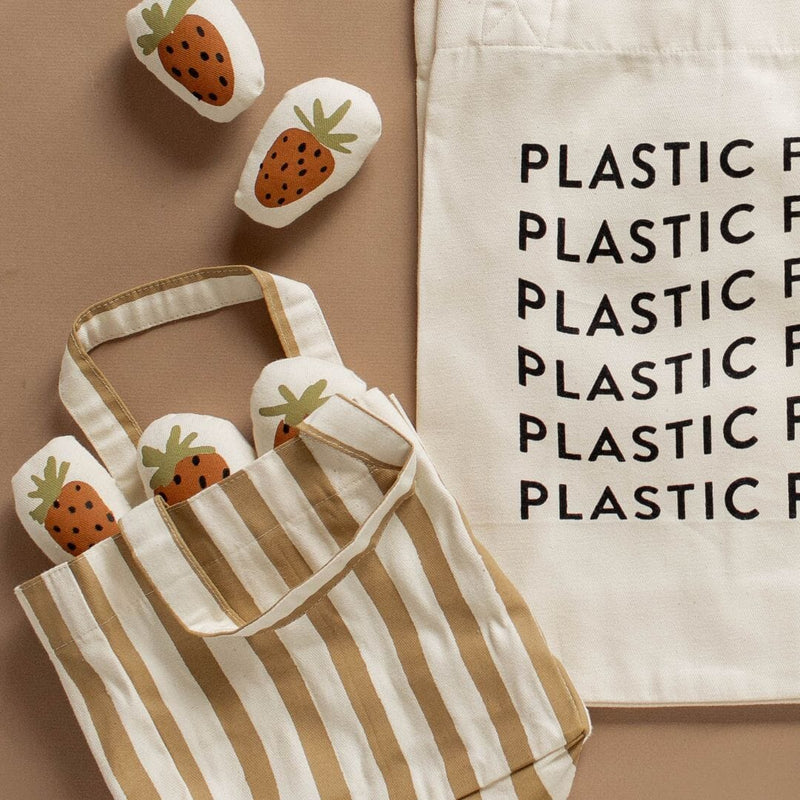 Striped tote bag filled with strawberry-print soft toys next to a canvas bag with "Plastic Free" text, eco-friendly shopping bags.