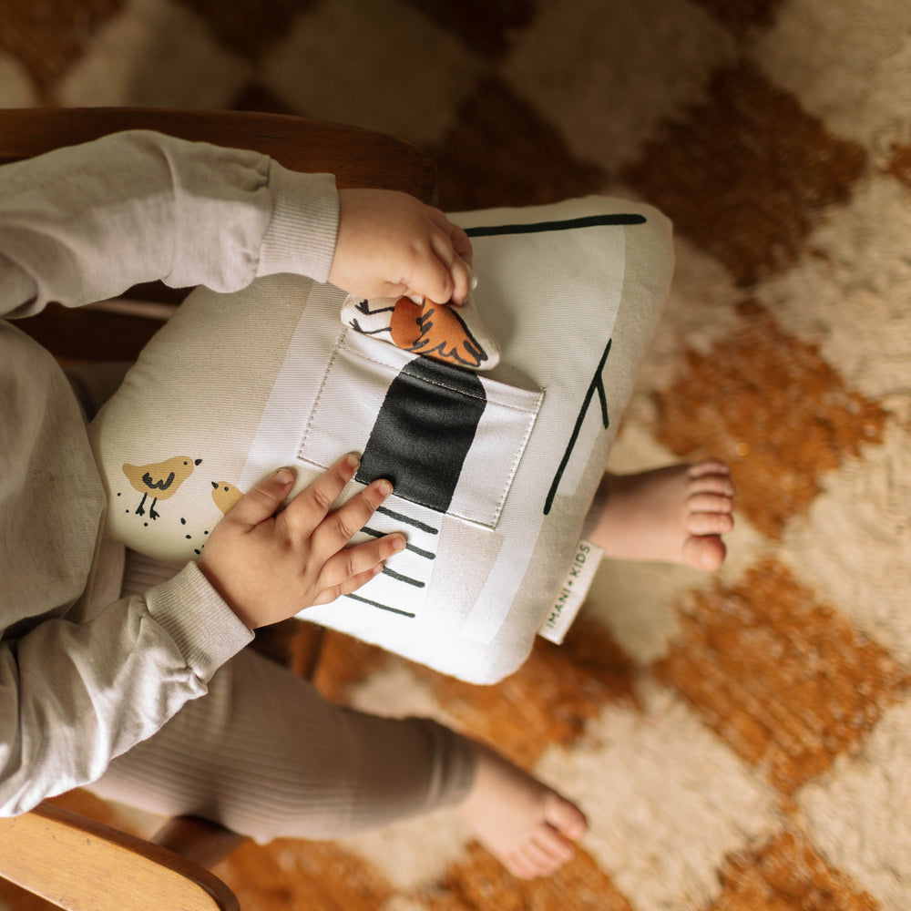 Toddler playing with a soft toy pillow in a cozy nursery room setting.