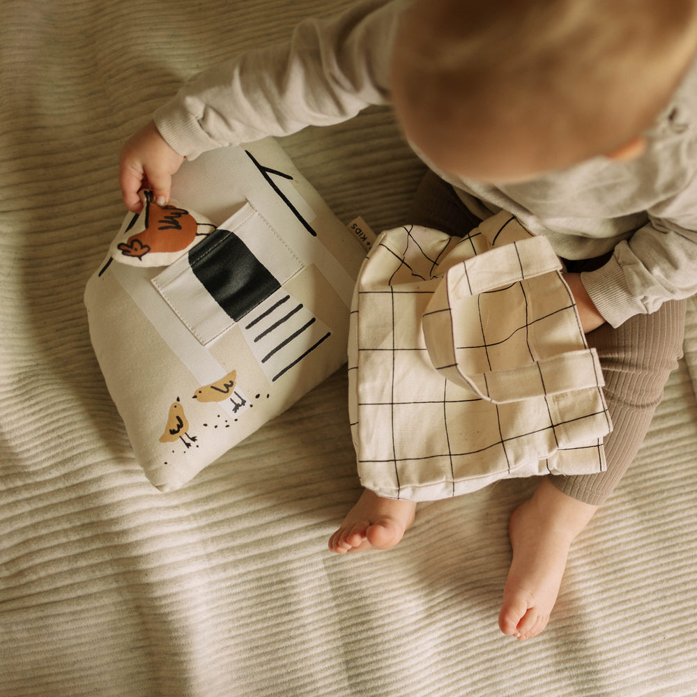 Baby sitting on a soft beige blanket holding decorative pillows, providing cozy nursery decor ideas.