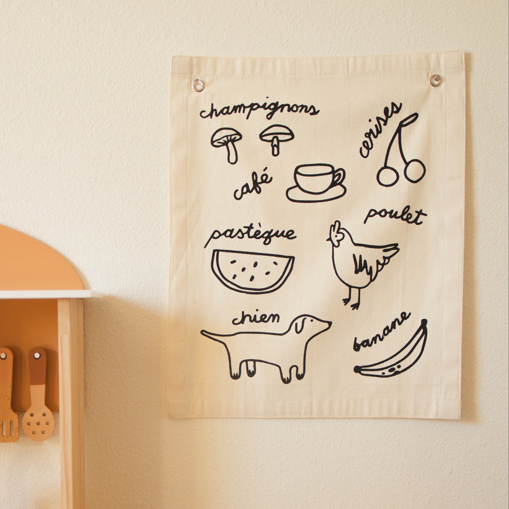 Decorative fabric wall hanging featuring simple black illustrations with French words like "champignons," "café," and "pastèque" for educational decor.