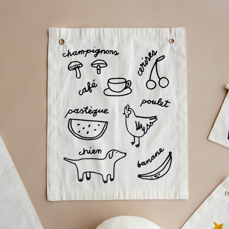 Fabric wall hanging with French food illustrations and text including mushrooms, cherries, coffee, watermelon, chicken, dog, and banana.