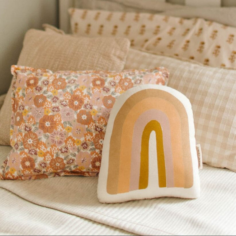 Cozy bedroom decor with floral pillow and rainbow cushion on pastel bedding.