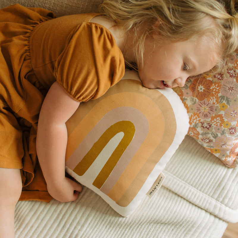 Child sleeping with rainbow-themed pillow on cozy bed with floral bedding.
