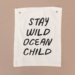 Canvas banner with motivational quote "Stay Wild Ocean Child" in bold black letters against a neutral background.