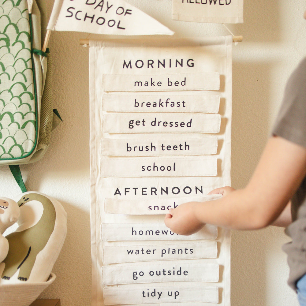 Child adjusting a fabric daily schedule chart with morning and afternoon activities for back-to-school organization.