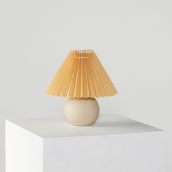 Cream table lamp with beige pleated shade on white pedestal, minimalist home decor.