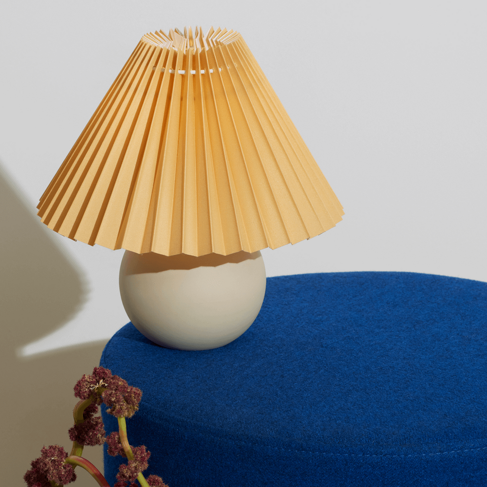 Elegant table lamp with a pleated lampshade on a blue surface.