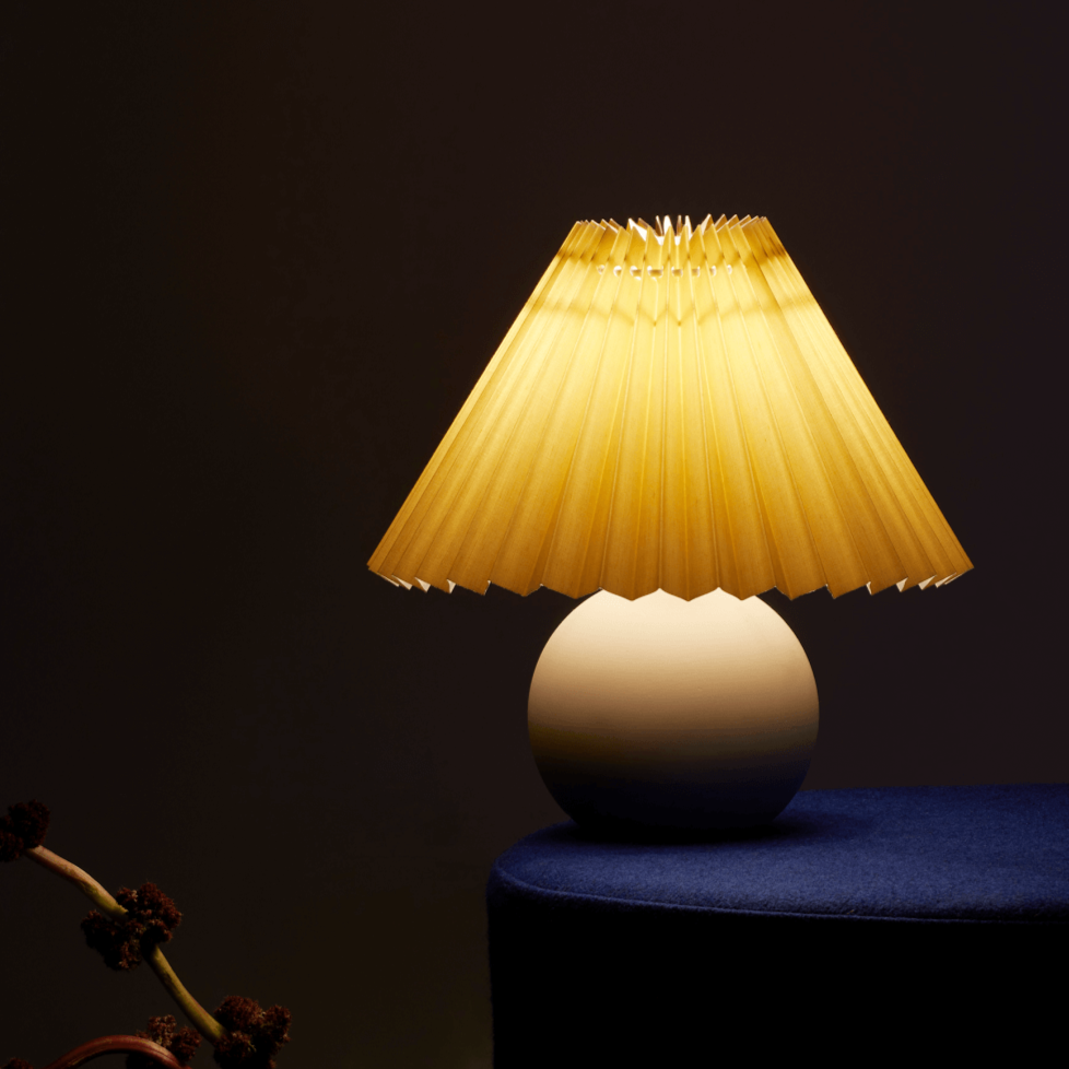 Modern table lamp with a pleated yellow lampshade on a dark background.