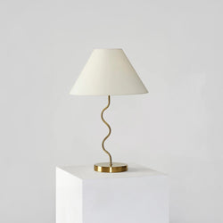 Stylish modern table lamp with a wavy gold stand and white lampshade on a minimalist pedestal, perfect for contemporary home decor.