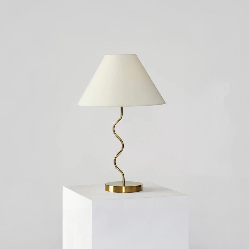 Stylish modern table lamp with a wavy gold stand and white lampshade on a minimalist pedestal, perfect for contemporary home decor.