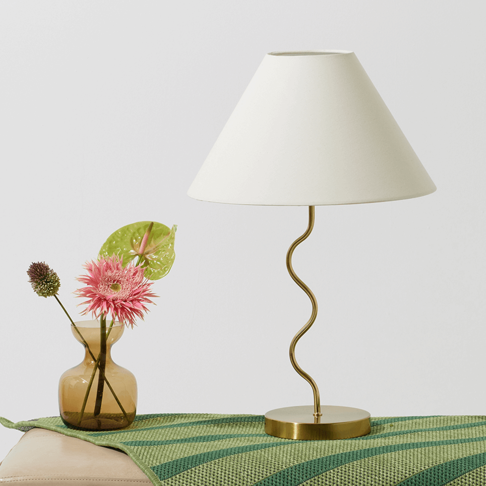 Stylish modern table lamp with a unique twisted metal stand and a white shade next to a decorative glass vase with vibrant flowers, perfect for contemporary home decor.