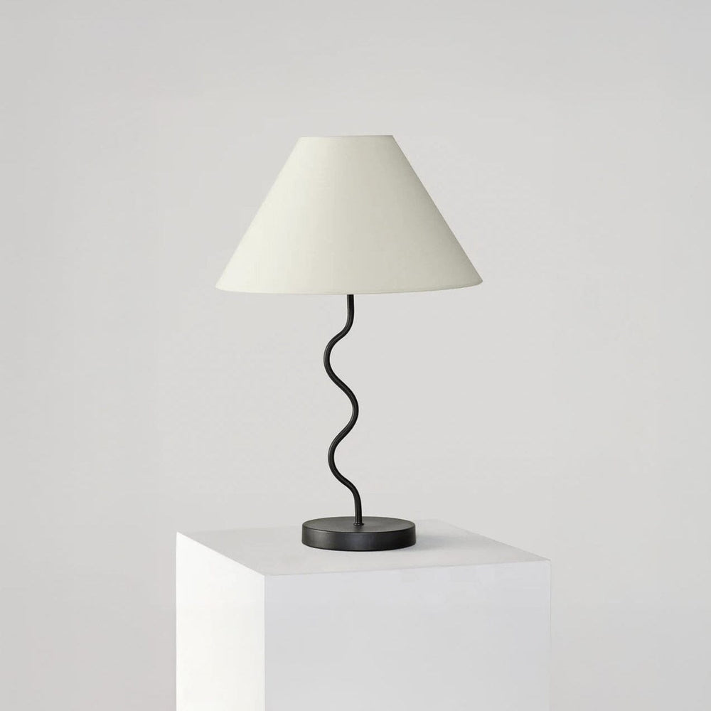 Modern black table lamp with a unique curved design and white lampshade on a white pedestal.