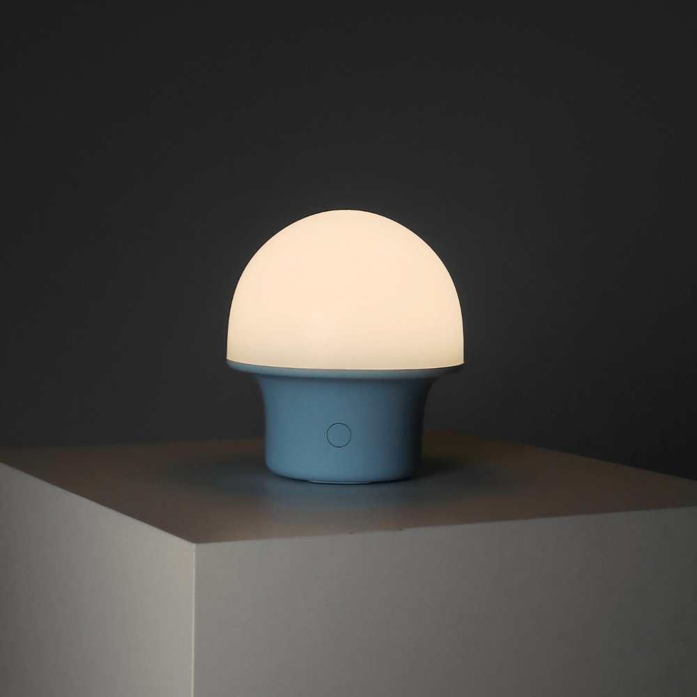 Modern minimalist table lamp with soft glow on a geometric surface in a dark setting.