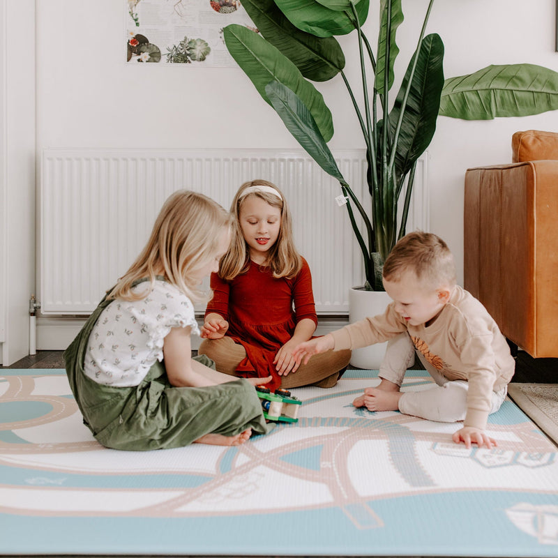 Children playing on a colorful play mat in a cozy living room setting.