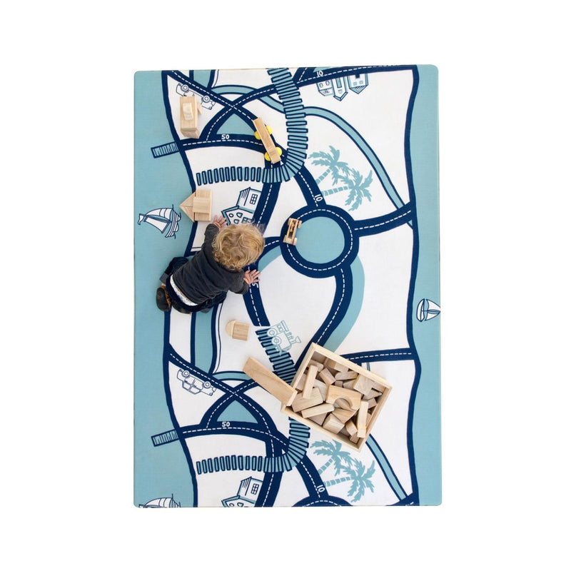 Toddler playing with wooden blocks on a decorative play mat featuring road and vehicle designs.