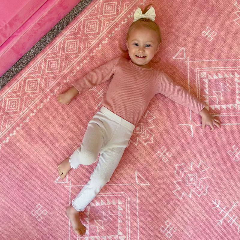 Smiling toddler girl lying on a decorative pink patterned rug.