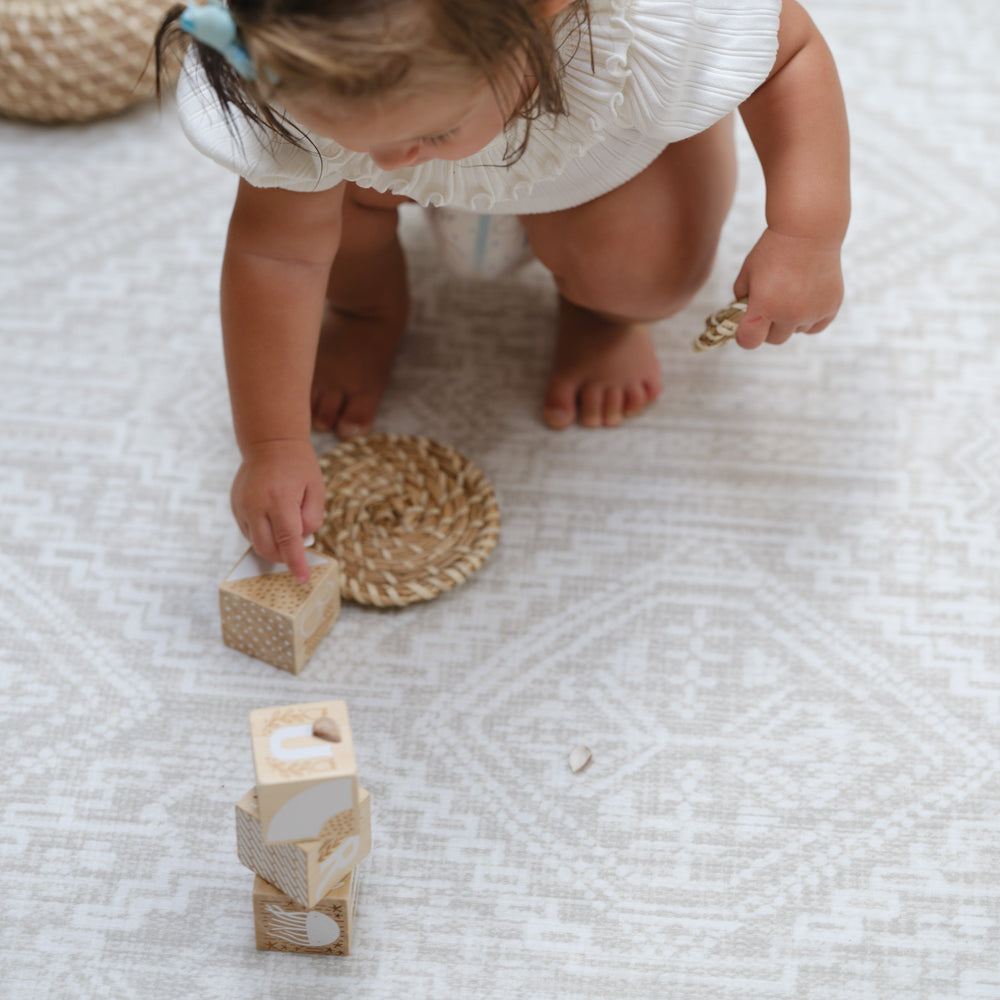 Toddler playing with wooden blocks on patterned rug.