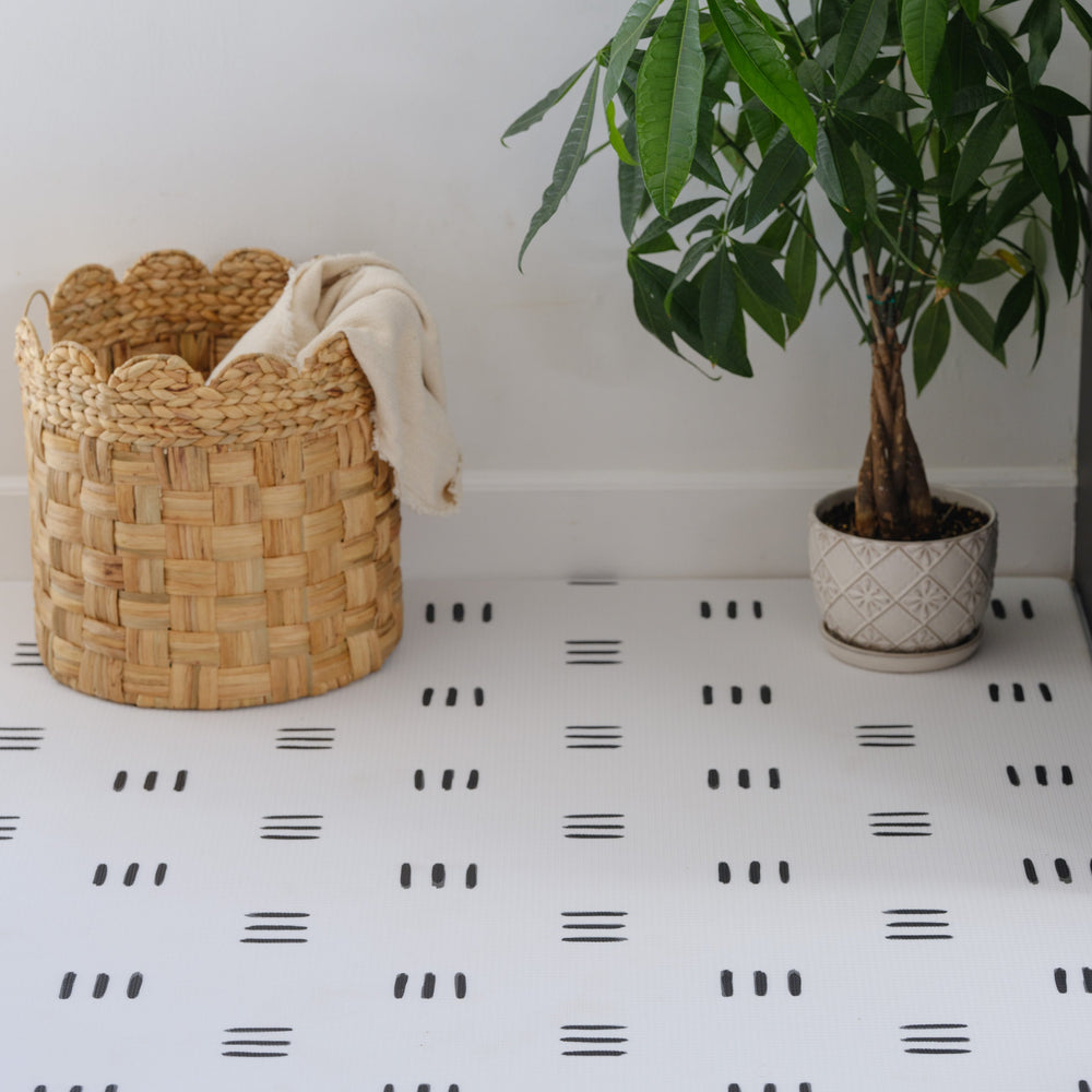Woven basket with blanket and potted indoor plant on modern patterned tile floor.