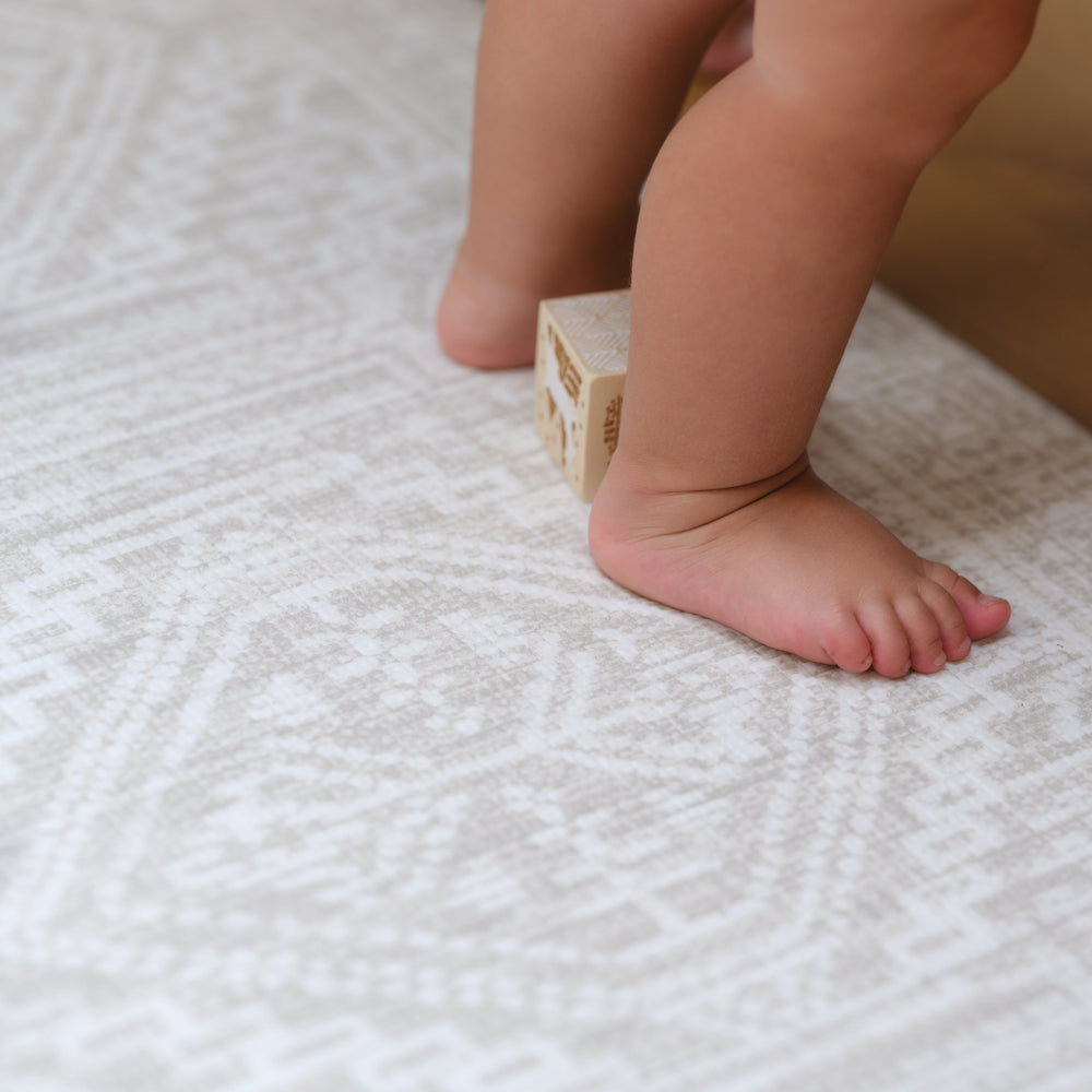 Toddler stepping on a soft patterned carpet with a wooden block.