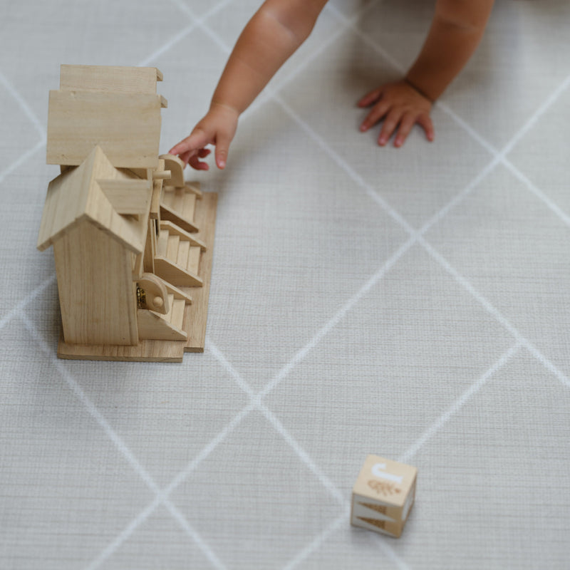 Child playing with wooden dollhouse on a gray patterned rug.