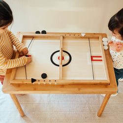 Children playing tabletop hockey game on a wooden table.
