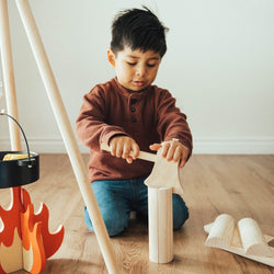 Young boy playing with wooden blocks and toy campfire indoors.