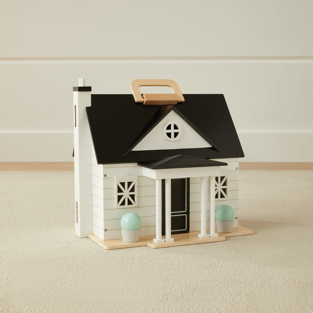Toy dollhouse with black roof and white walls on a beige carpeted floor.