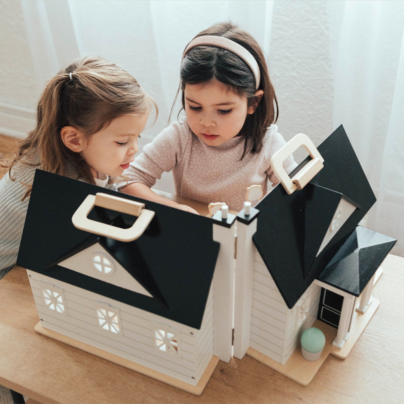 Two young girls playing with a wooden dollhouse in a cozy room setting.
