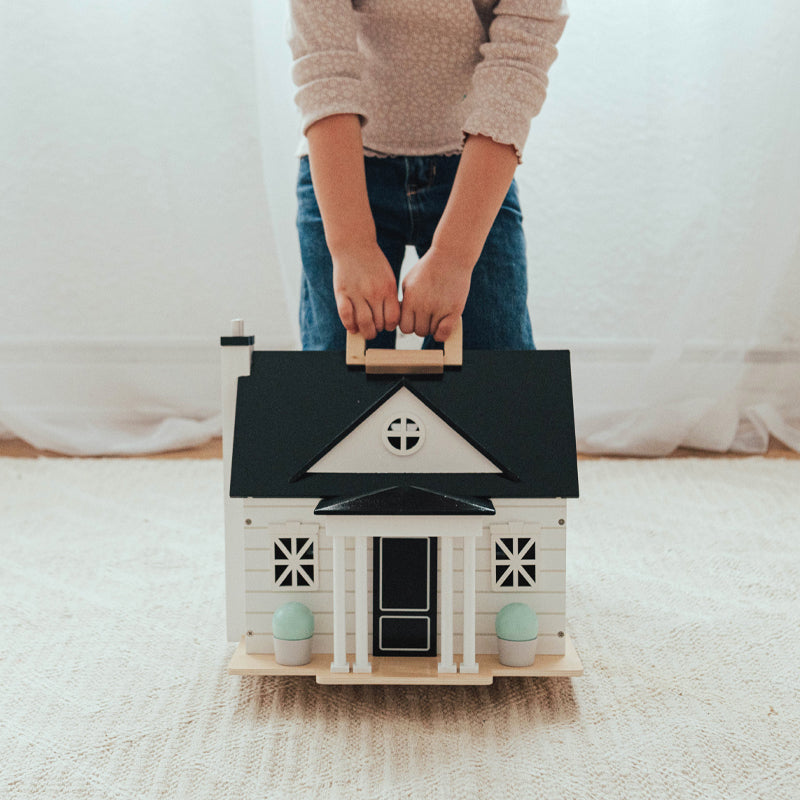 Child holding a wooden toy dollhouse with black roof and white walls.