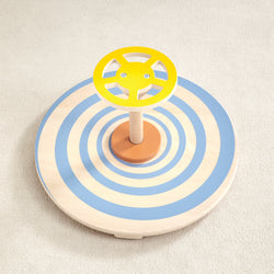 Wooden spinning toy with yellow steering wheel and blue concentric circles on beige carpet.
