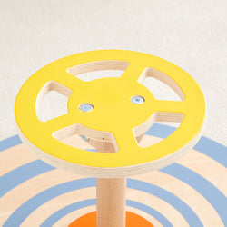 Bright yellow wooden toy steering wheel on a playful multicolored background, highlighting children's playroom decor.