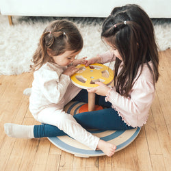 Two young children playing with a wooden balance board in a cozy home setting.