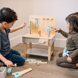 Children playing with a wooden toy tool bench in a playroom.