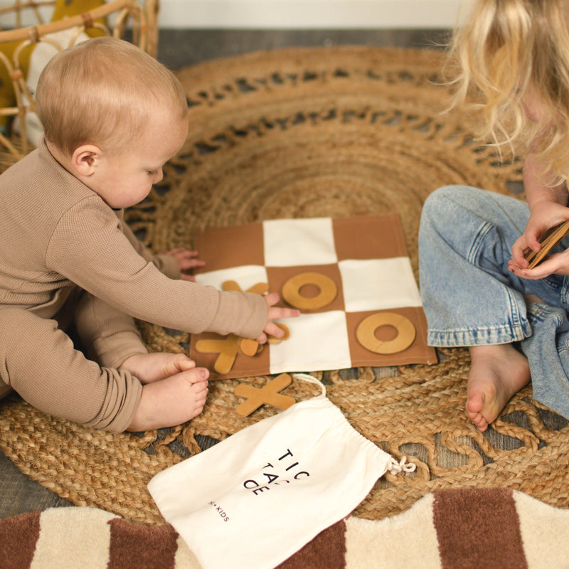 Children playing tic-tac-toe on a woven rug.