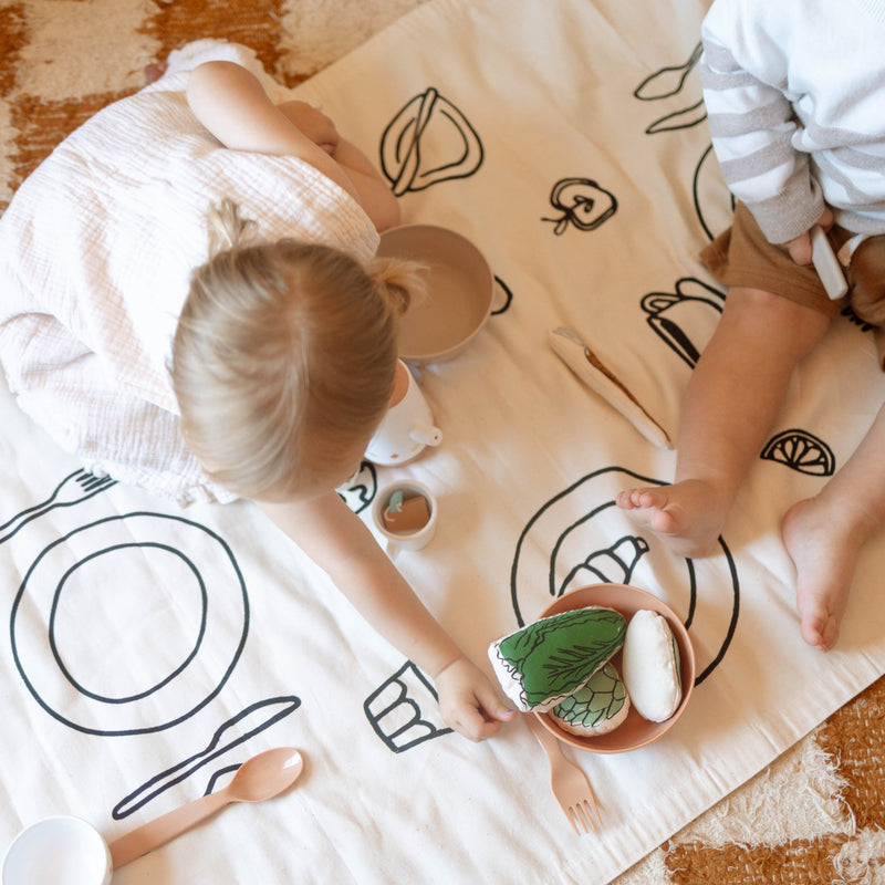 Children playing with toy food on a decorative play mat.