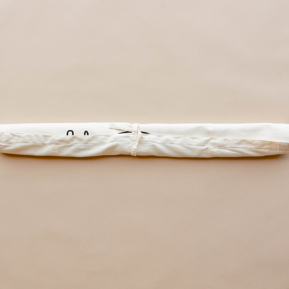 White fabric yoga mat bag with tie closure on neutral background.