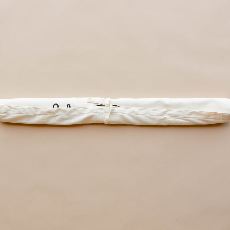 White fabric yoga mat bag with tie closure on neutral background.