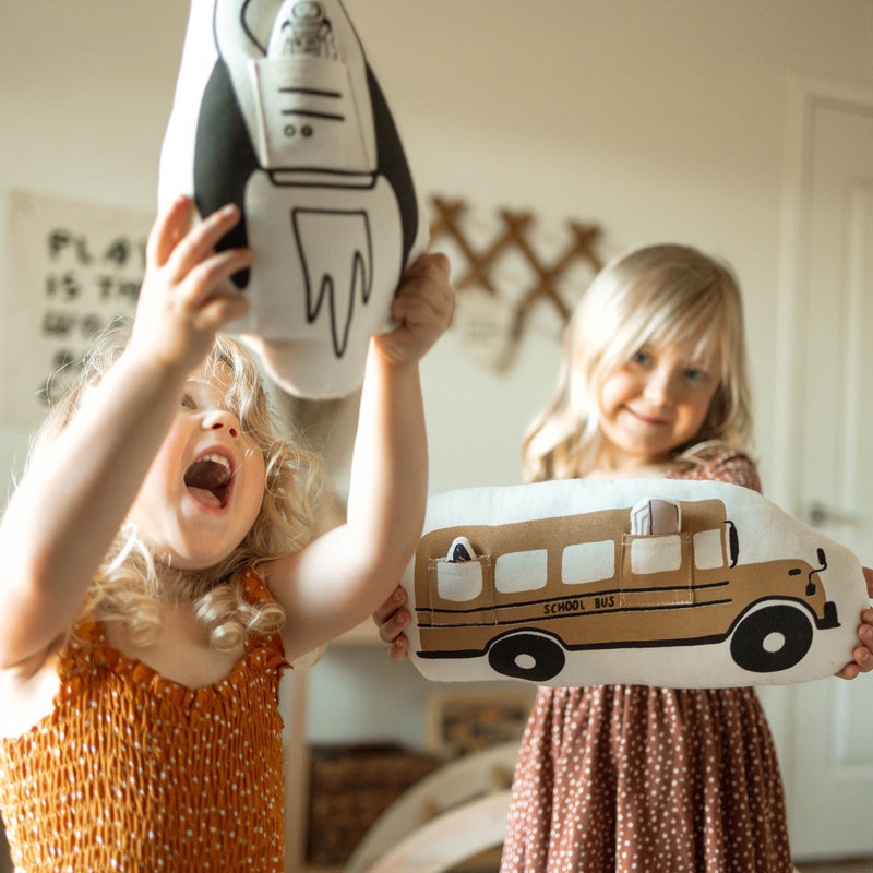 Children playing with educational rocket and school bus plush toys indoors.
