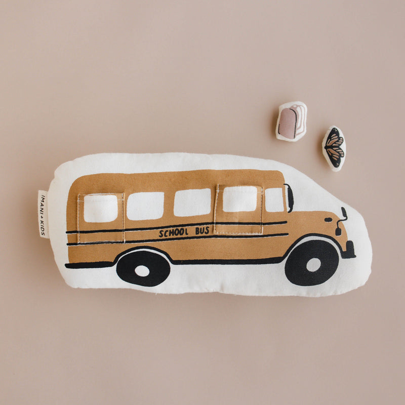 Soft school bus plush toy on a beige background with butterfly and backpack accessories nearby.