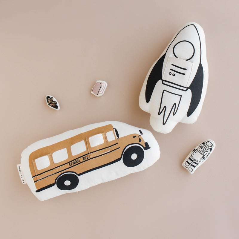 Plush rocket and school bus toys with astronaut and butterfly on beige background.
