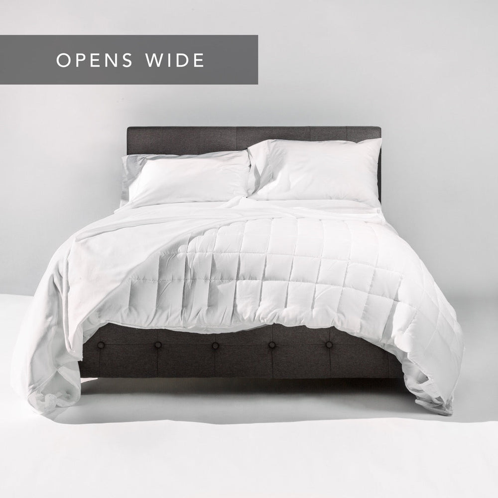 King-sized bed with white comforter and pillows on dark upholstered headboard in minimalist bedroom design.