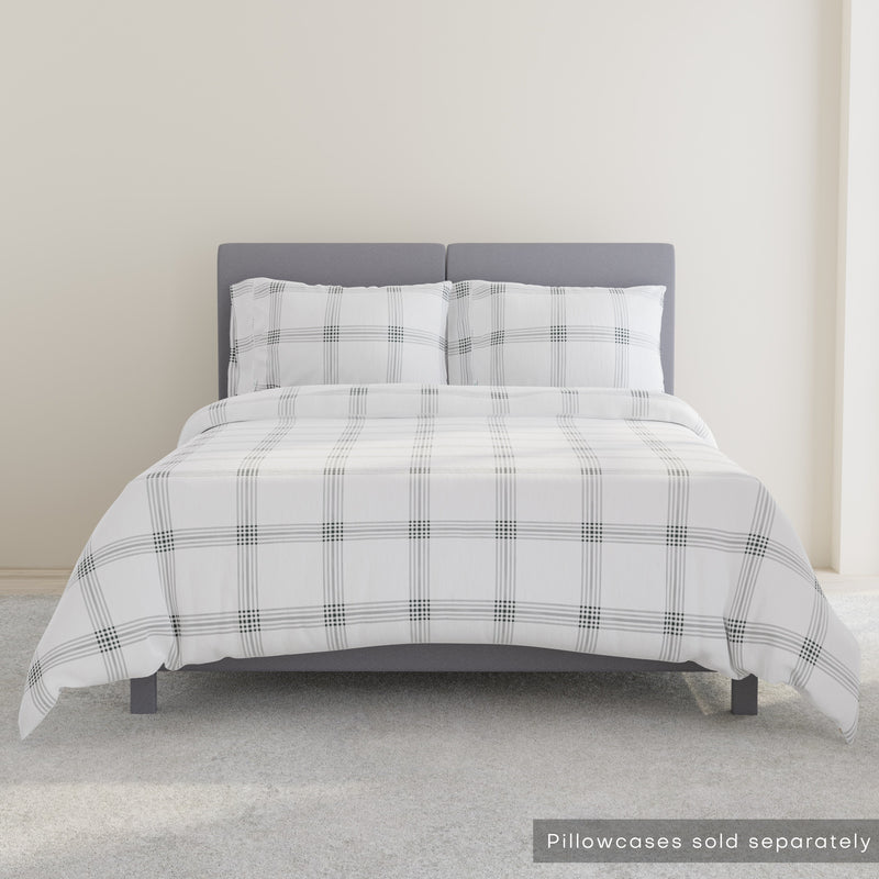 Gray upholstered bed with white and gray plaid bedding in a minimalist bedroom setting.