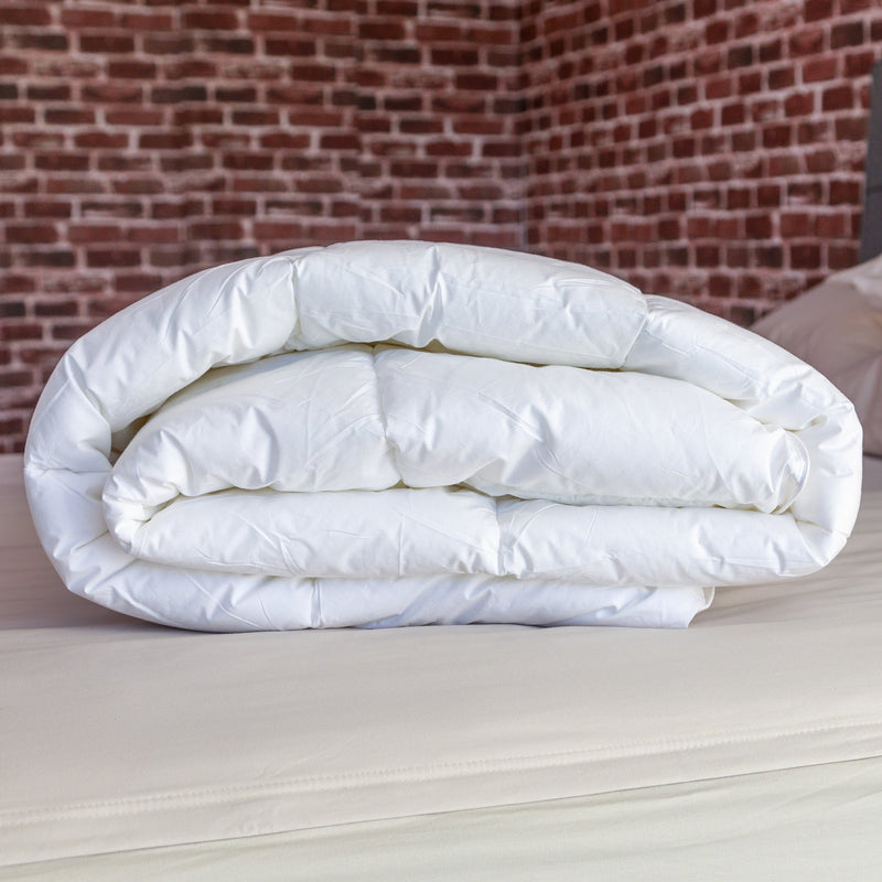 Folded white duvet on a bed with exposed brick wall background.