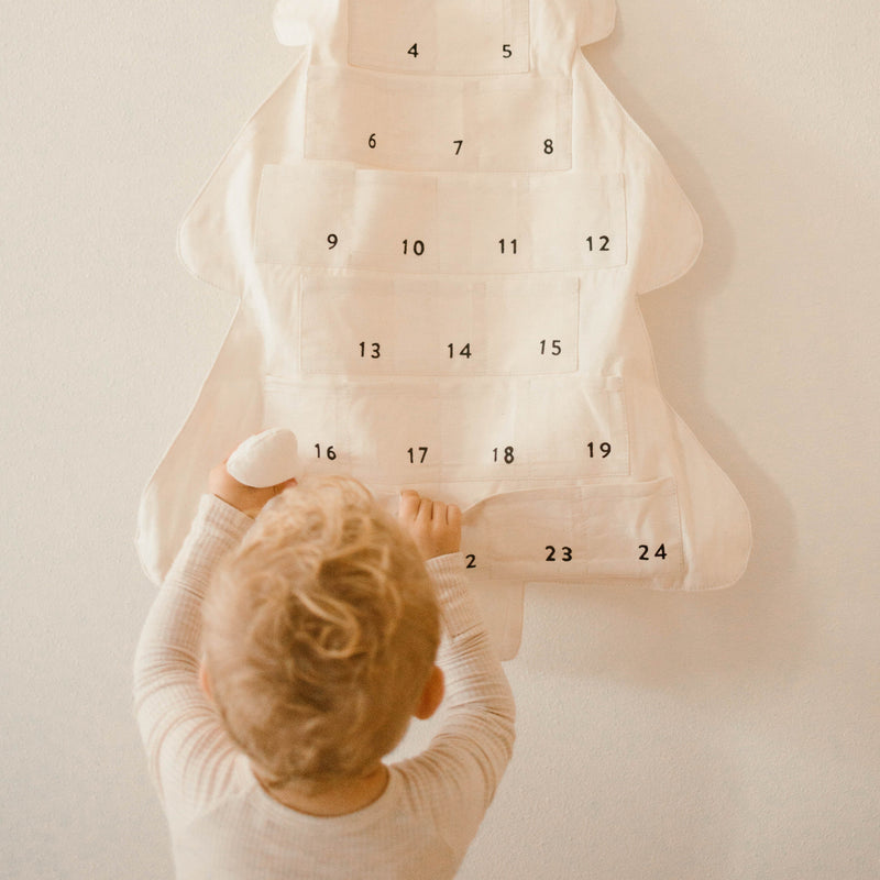 Toddler interacting with fabric advent calendar on white wall.