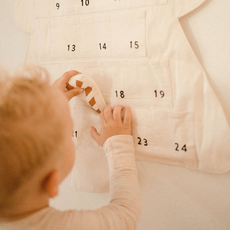 Child interacting with a fabric advent calendar with numbered pockets for countdown activities.