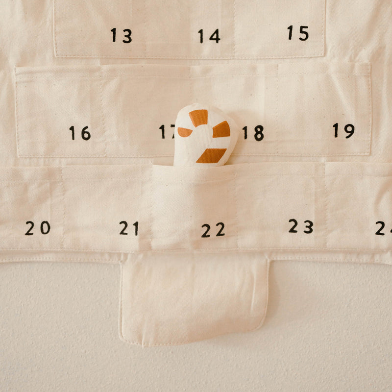 Cloth advent calendar with numbered pockets and a small stuffed toy in one pocket.