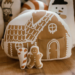 Stuffed gingerbread house pillow with candy cane and gingerbread man decorations, perfect for cozy holiday decor.